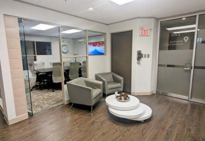 Bright waiting area with two grey armchairs, a tiered white coffee table, and views into a meeting room.