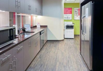 Office kitchen area with grey cabinetry and stainless steel refrigerator.