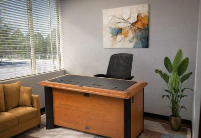 Compact office suite with a wood-finished desk, tan sofa, and decorative wall art.