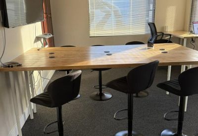 Long communal high-top wooden work table with bar stools and wall-mounted TV.