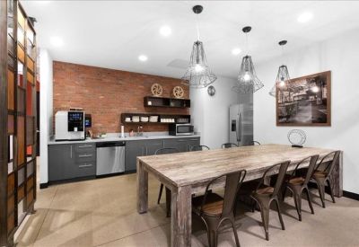 Modern communal kitchen and dining area with an exposed brick wall and large rustic table.