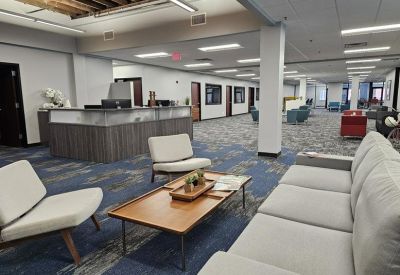 Spacious lobby lounge with modern grey sofa, wooden coffee table, and a reception desk in the background.