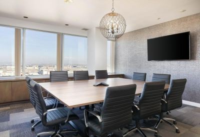Sun-drenched boardroom with a large wooden table, black leather chairs, and expansive city views.