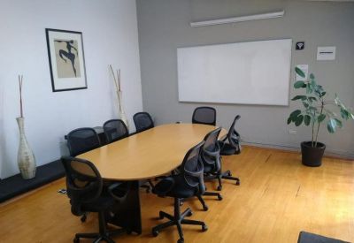 Spacious meeting room with an oval wooden table, black mesh chairs, and a large whiteboard.