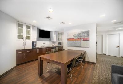 Communal break area with a large wooden dining table, modern cabinetry, and a wall-mounted television.