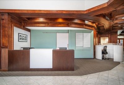 Professional reception area with a dark wood desk, sage green accent wall, and decorative overhead woodwork.