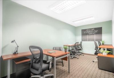 Shared office space featuring multiple wooden desks, ergonomic black chairs, and a motivational wall graphic.