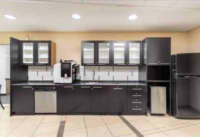 Modern office kitchen with dark cabinetry, coffee machine, and stainless steel dishwasher.