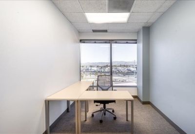 Bright private corner office with an L-shaped desk and city views.