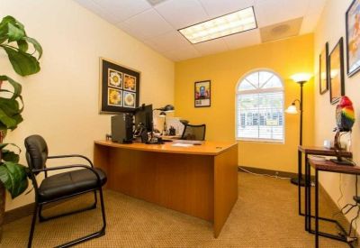 Private office suite with a wooden desk, guest chair, and natural light from an arched window.
