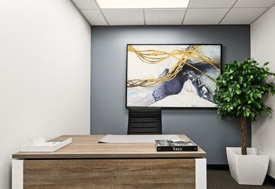 Private office featuring a wooden desk, abstract art, and a potted green tree.