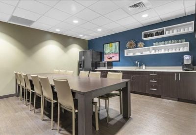 Communal breakroom with a large dining table, navy blue accent wall, and kitchenette.