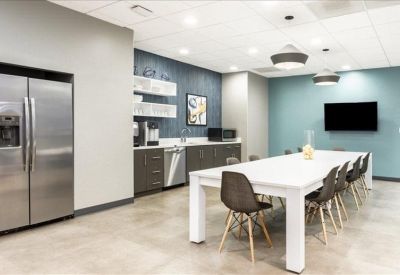 Bright kitchen and breakroom area with a long white dining table and teal feature wall.