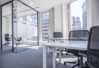 Modern meeting space with glass partitions and white desks overlooking city buildings.