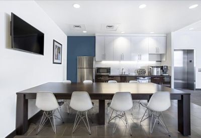Modern communal kitchen and dining area with white cabinetry and stainless steel appliances.