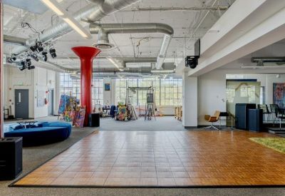 Open coworking space with a wooden dance floor and industrial ceiling.