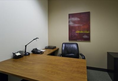 Private office featuring a wooden L-shaped desk, leather chair, and warm wall art.