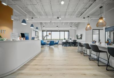 Open-plan coworking space with a white breakfast bar, cafe seating, and industrial ceiling.