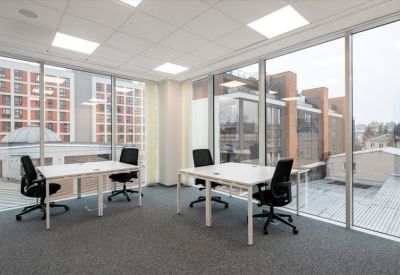Corner office suite with white desks and floor-to-ceiling windows showing urban views.