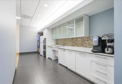 Clean communal kitchen area with white cabinetry, coffee station, and stone backsplash.