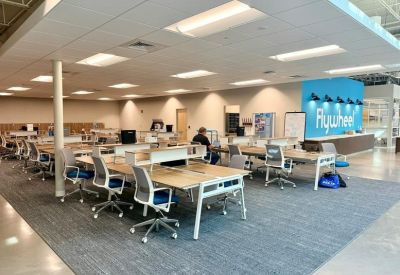 Open-plan office with multiple workstations and a branded blue reception wall in the background.