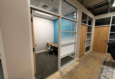 Private glass-walled office with a wooden desk and a blue accent wall.