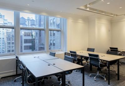 Open-plan workspace with multiple desks and large windows overlooking city buildings.