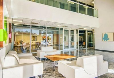 Spacious sunlit lobby with white modern sofas, a wooden coffee table, and polished stone flooring.