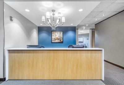 Reception desk with light wood paneling under a modern chandelier.