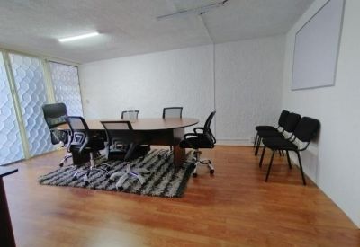 Spacious meeting room featuring an oval wooden table, black mesh chairs, and warm wood flooring.