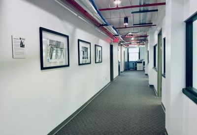 Long office corridor with framed artwork and industrial ceiling pipes.