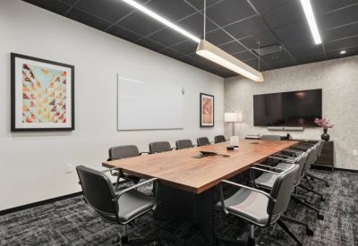 Professional boardroom with a large wood table, black leather chairs, and integrated media screen.