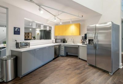 Modern communal kitchen with grey cabinetry, yellow accents, and stainless steel appliances.
