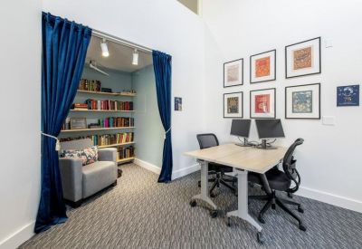 Cozy reading nook with blue curtains and a nearby workstation with dual monitors.