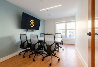 Bright meeting room with a large screen, conference table, and mesh ergonomic chairs.