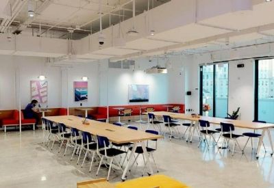 Open-plan coworking space with long wooden communal tables and black chairs.