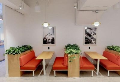 Modern dining booths with orange cushions, light wood tables, and indoor plants.