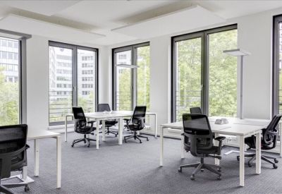 Spacious open-plan office with black ergonomic chairs, white desks, and large windows overlooking trees.