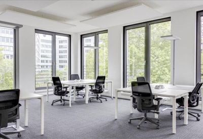 Light-filled open-plan office featuring white workstations and black mesh chairs by large windows.