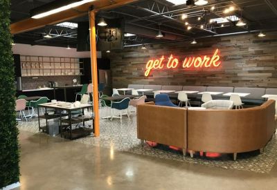 Large communal lounge with a neon get to work sign on a wood-paneled wall.