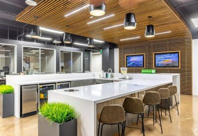 Modern office kitchen with a white marble island, wood-slat ceiling, and bar stool seating.