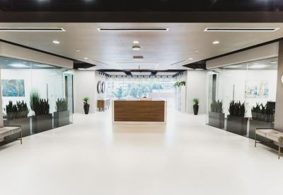 Spacious reception lobby with a wooden front desk, white flooring, and glass-walled side offices.