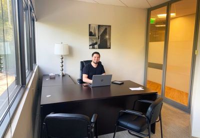 Man at a modern private office desk with a large window and guest seating.