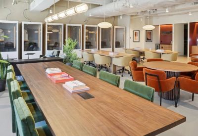 Spacious coworking area with long wooden tables, colorful chairs, and private phone booths.