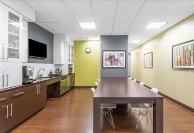 Modern communal kitchen and breakout area with a long wooden dining table and lime green accent wall.