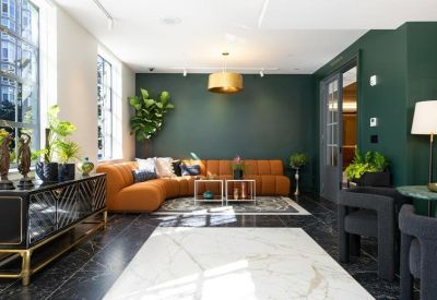 Spacious lounge with a curved orange sofa, green accent wall, and marble flooring.