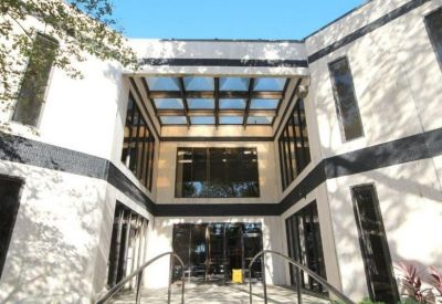 Bright glass-roofed atrium entrance with a symmetrical white facade and black horizontal accents.