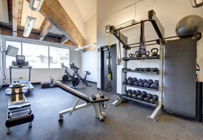Industrial-style gym with treadmills, rowing machines, and weight racks under vaulted ceilings.