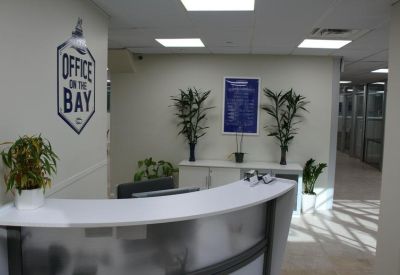 Curved white reception desk in a bright lobby featuring potted plants and branded wall signage.