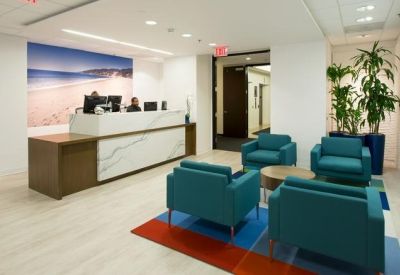Reception area with marble-fronted desk and teal armchairs over a colorful rug.